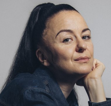 Eine Person mit langen dunklen Haaren stützt das Kinn in die Hand