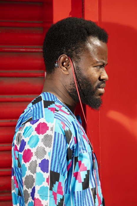 Seitenansicht einer farbigen Person, die einen Bart und ein buntes Shirt trägt und rote Ohrstöpsel-Kopfhörer über das Ohr gelegt hat