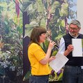 Zwei Personen stehen vor Fotos mit Pflanzenmotiven - eine hält ein Mikro, die andere eine Publikation